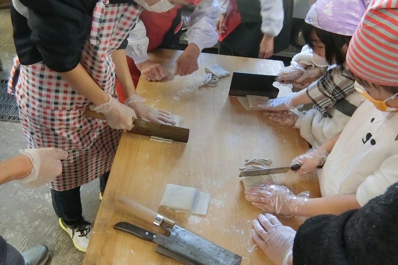 みんなでそばを包丁で切っている