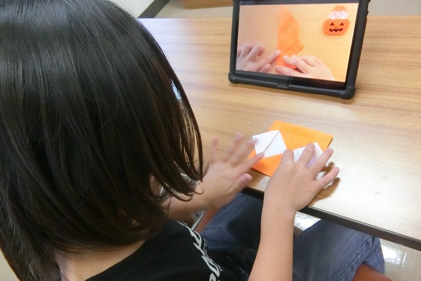 タブレットを見ながら折紙を折っている