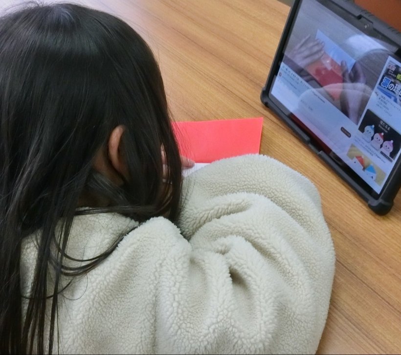 タブレットを見ながら折り紙を折っている