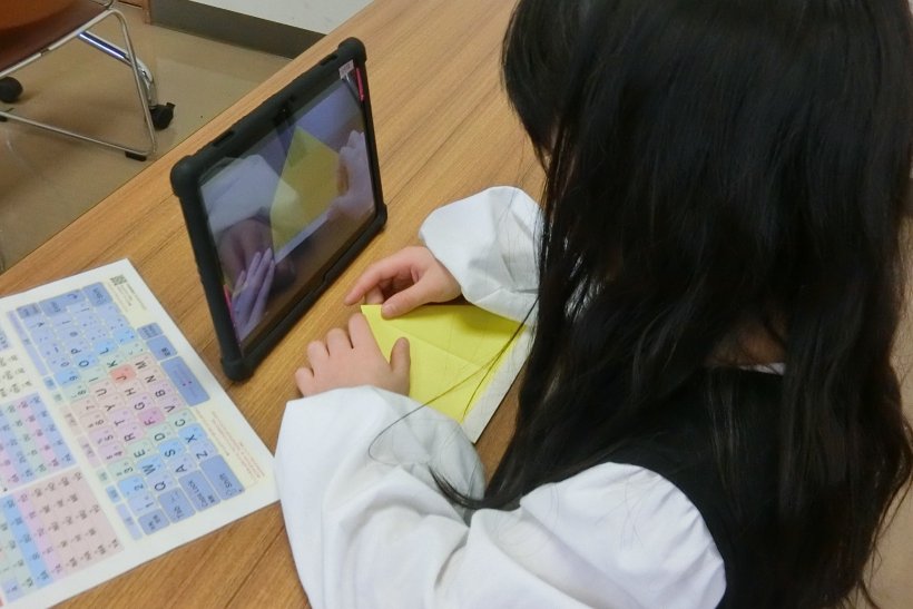 タブレットを見ながら折り紙を折っている