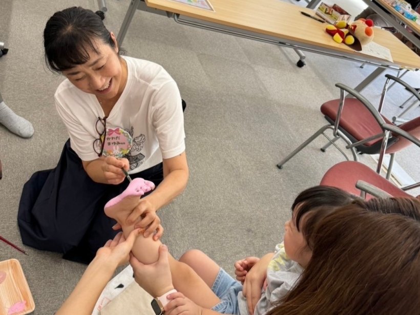 抱っこされた足裏に絵の具を塗っている