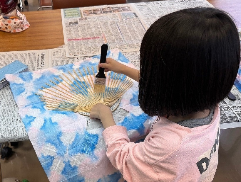 うちわの骨にのりを塗っている