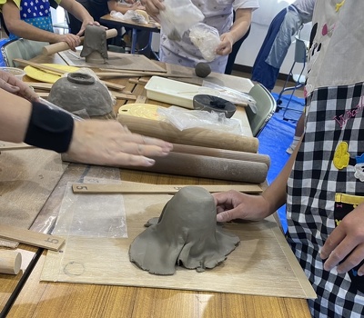 子どもがコップを作る過程で粘土を型に沿わせている様子。横で濵田先生が指示している。