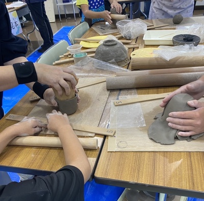 子どもがコップを作る過程で粘土を型に沿わせている様子。横で濵田先生が補助している。