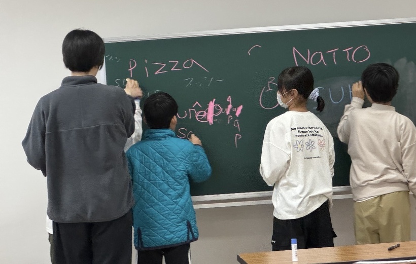 黒板へみんなで英語のスペルを書いている