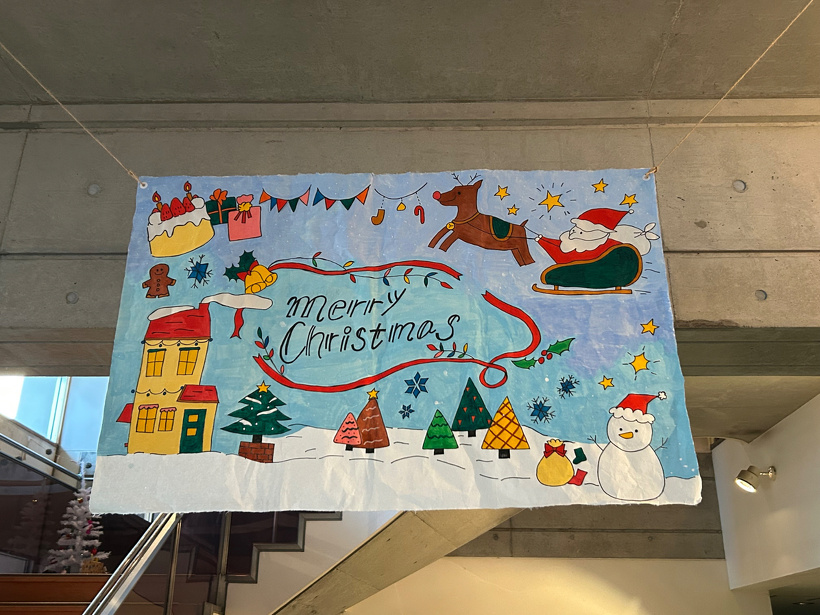 クリスマスのイラストを描いた和紙を2階の手すりから吊るしている