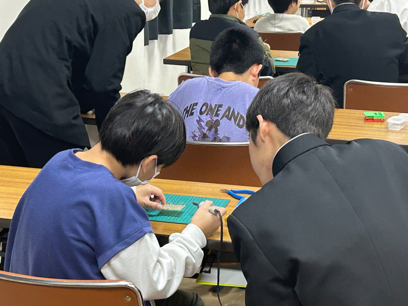 参加者の小学生が高校生と一緒にはんだづけをしている様子