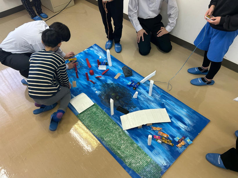参加者の小学生が作った車型ロボットを操作してコースを走らせている様子