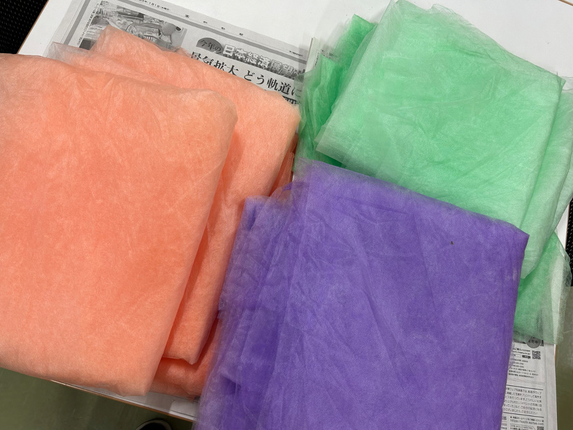 オレンジ、紫、緑に染まった不織布を折りたたんで並べている
