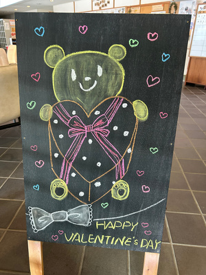 黒板の立て看板にハート型のプレゼント箱を持ったクマを描いている