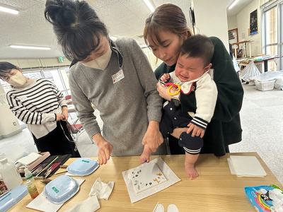 川田先生が絵の具の付いた子どもの足の裏をタイルに押し付けている