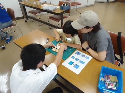 親子で金ノコギリで木材を切っています。高校生がサポート中。